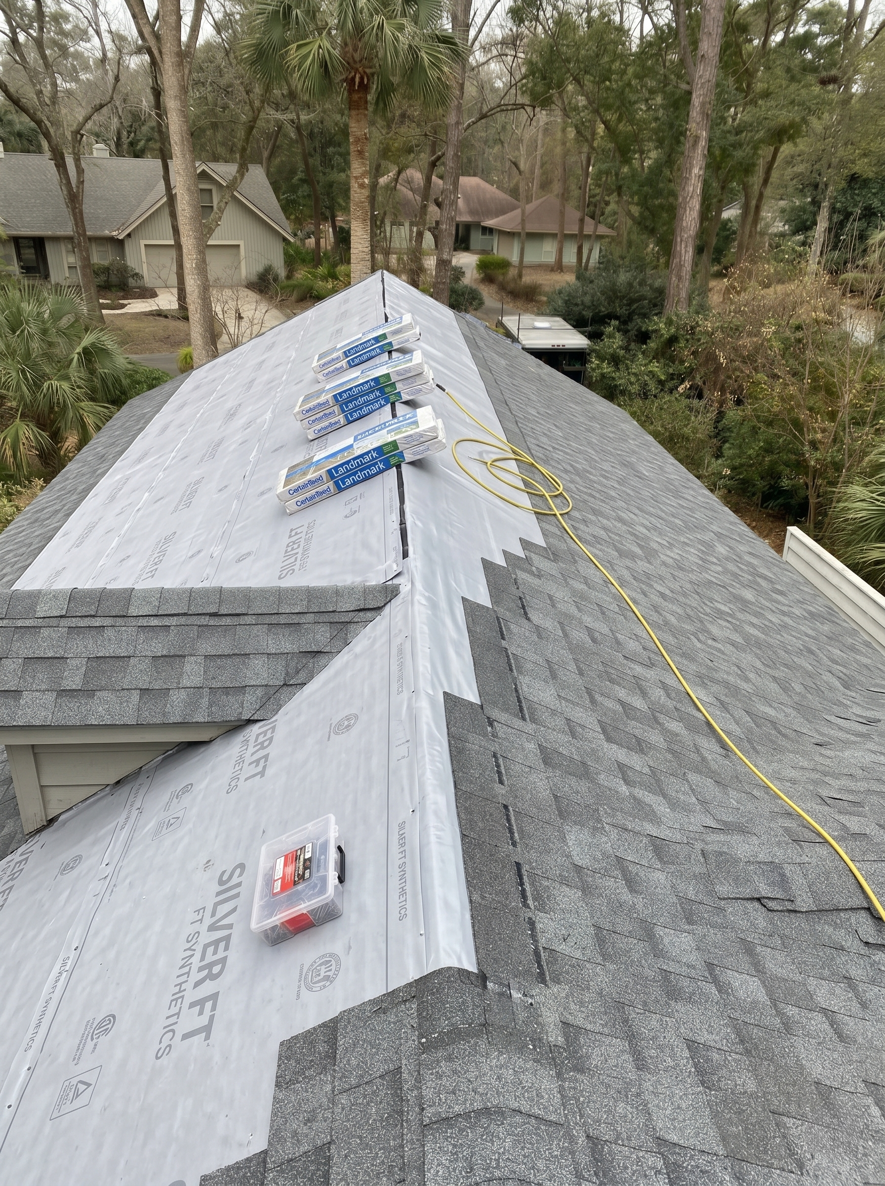 Roof mid-tear-off: synthetic underlayment laid down, CertainTeed Landmark shingle bundles staged on the ridge