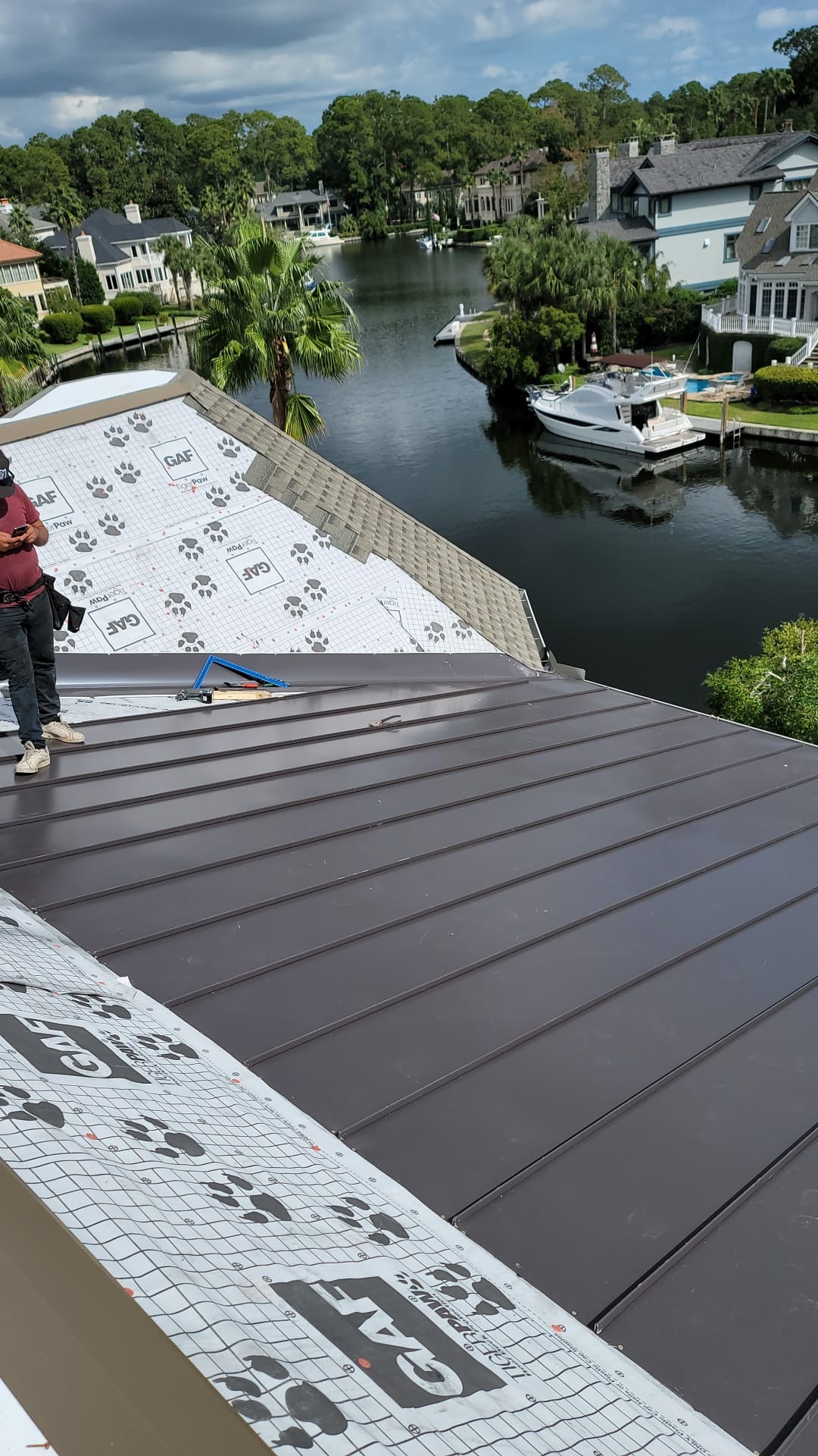 Aerial view of a standing-seam metal roof on a Lowcountry plantation home, marsh and palms behind